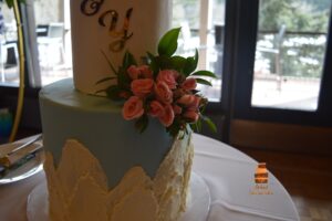 Tall two-tier buttercream wedding cake with fresh blush pink roses and leaves, decorated with custom cake topper, filled with chocolate ganache and decorated with mountain patterns on the side, delivered and setup to Calgary waterfront park, by Afsheed Cakes