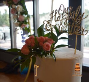 Close-up of Custom Cake topper, blush pink roses and greenery on a white wedding cake