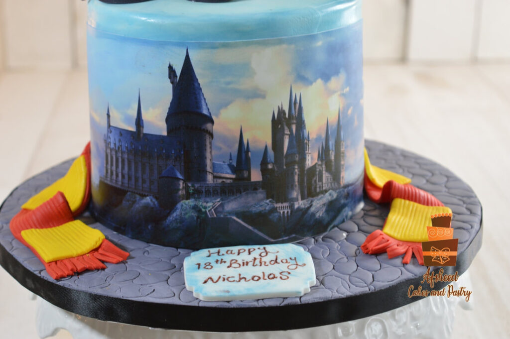 Zoomed in on the hand made birthday sign and an edible print of Hogwarts, on a small Harry Potter–themed birthday cake showing Gryffindor scarf and crest in, Created by Afsheed Cakes and Pastry in Calgary