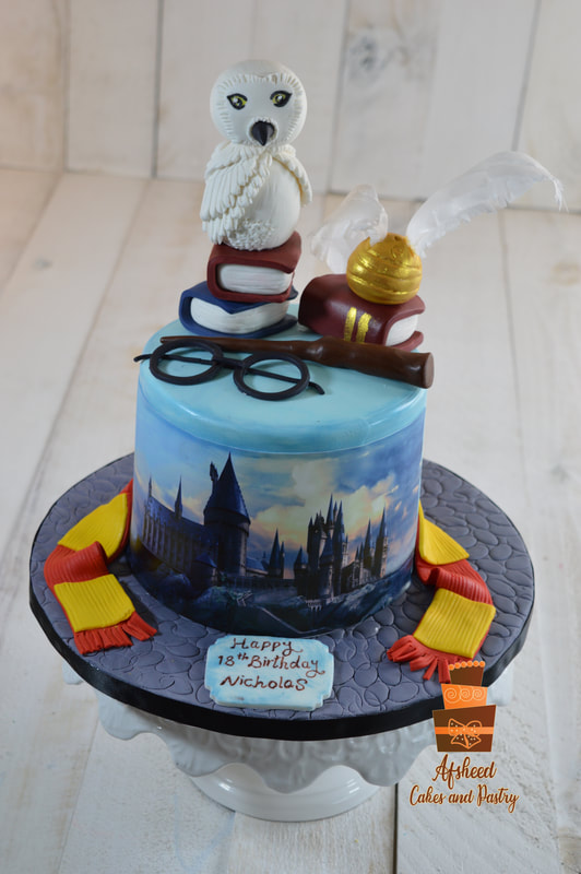 A small Harry Potter–themed birthday cake decorated with hand made owl, golden snitch, wand, Gryffindor scarf and crest in Gryffindor colors with with an edible image of the Hogwarts on the side of the cake , created by Afsheed Cakes and Pastry in Calgary