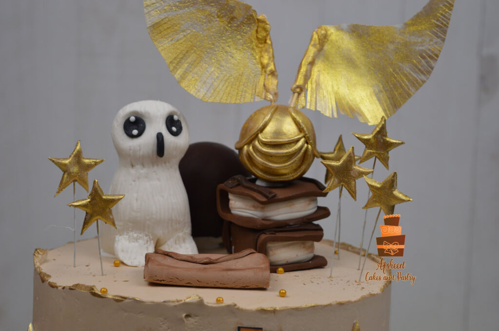 zoomed in view of A Harry Potter birthday cake showing hand made edible owl, spell books, edible golden snitch, edible gold stars, hand made Hogwarts invite letter on a butter cream delicious cake made by Afsheed Cakes and Pastry in Calgary