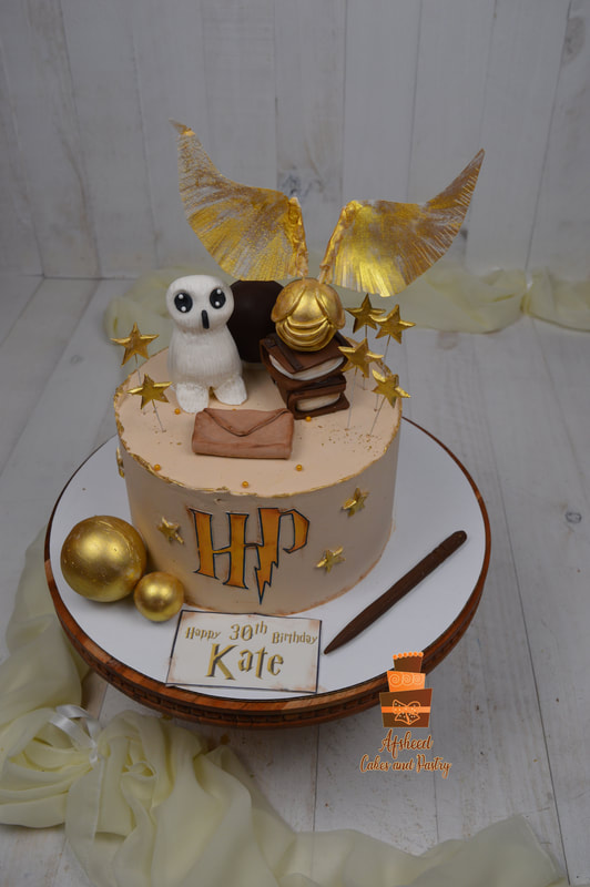A Harry Potter birthday cake decorated with a hand made edible owl, spell books, edible golden snitch, edible gold stars and balls, hand made Hogwarts invite letter with edible gold HP logo , Wand, all on a butter cream delicious cake made by Afsheed Cakes and Pastry in Calgary