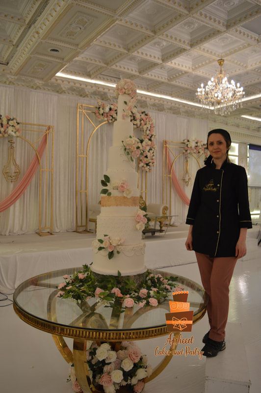 Grand multi-tier wedding cakes Calgary - Majestic seven-tier white fondant wedding cake featuring intricate lace detailing, gold bands, and cascading blush roses delivered to Empire Banquet Hall to serve over 400 guests by Afsheed cakes, in Calgary for couples planning an extravagant, large-scale luxury wedding celebration.
