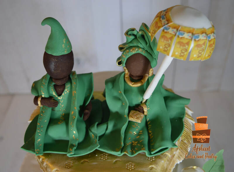Custom Nigerian or African themed wedding cakes Calgary - Three-tier white fondant wedding cake featuring traditional Nigerian African hand made toppers in green Gele and Fila attire with ceremonial kola nuts by Afsheed cakes, in Calgary for couples celebrating a Nigerian traditional marriage or West African heritage.