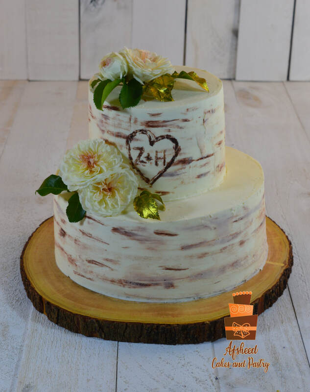 Two tier wedding cake decorated with fresh dahlias and edible gold, decoration matches forest theme and aspen trees, on a wooden slab tray